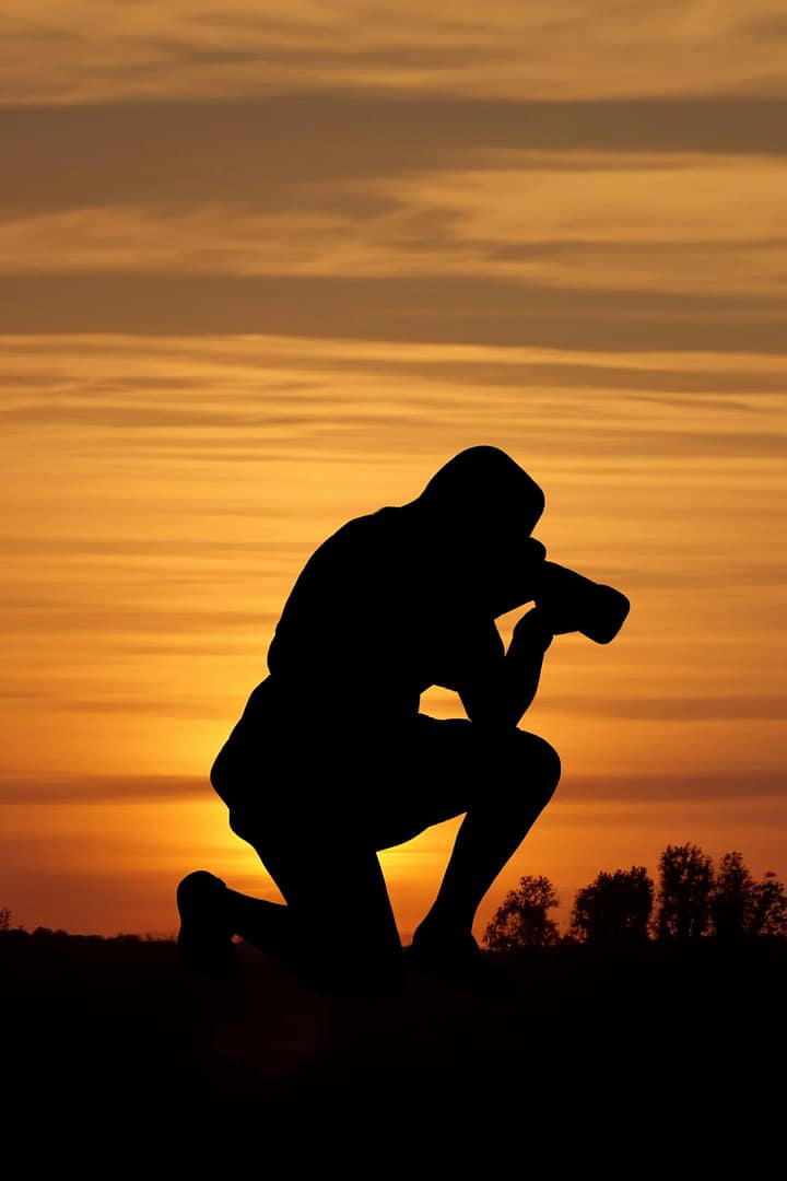 A silhouette of a photographer knelt down against a sunset